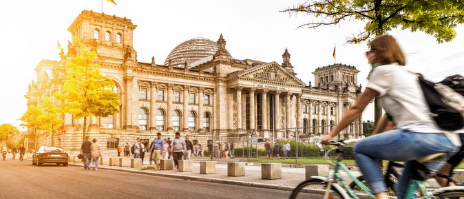 Eine Frau fährt bei Sonnenschein auf dem Fahrrad am Berliner Bundestag vorbei