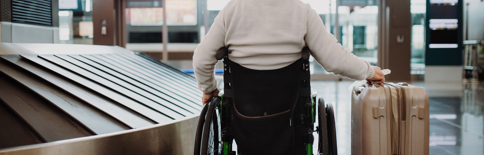 Mann im Rollstuhl schiebt seinen Koffer am Flughafen