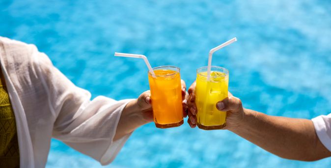 Zwei Hände stoßen mit Gläsern über einem Pool an