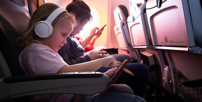 Ein Kind im Flugzeug trägt Kopfhörer und bedient ein Tablet