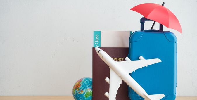 Auf einem Tisch steht ein Miniaturkoffer, Flugzeug und eine kleine Weltkugel mit einem Reisepass und einem Flugticket
