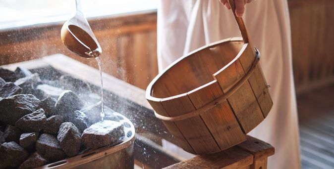 Ein Mann gießt Wasser auf heiße Steine in einer Sauna