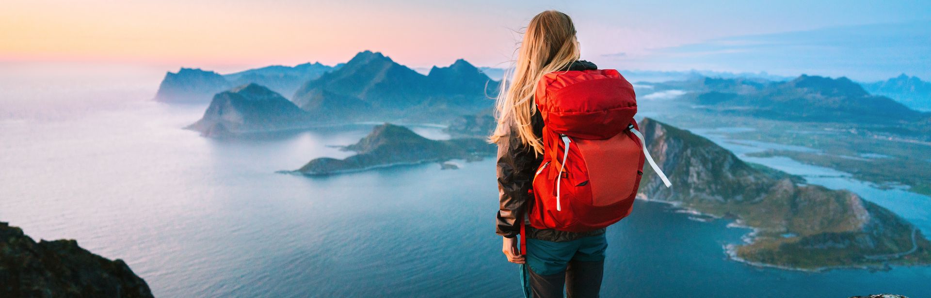 Alleinreisende Frau mit Rucksack schaut von einem Berg auf Wasser 