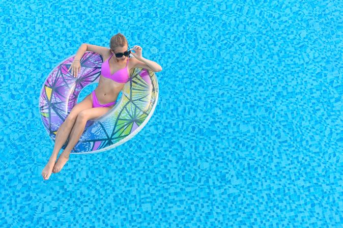 Eine Frau in einem pinken Bikini sitzt in einem Pool in einem bunten Poolfloatie