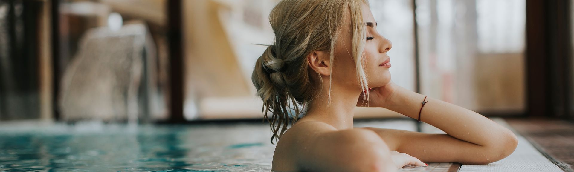 Frau lehnt am Rand eines indoor Pools und hat die Augen geschlossen