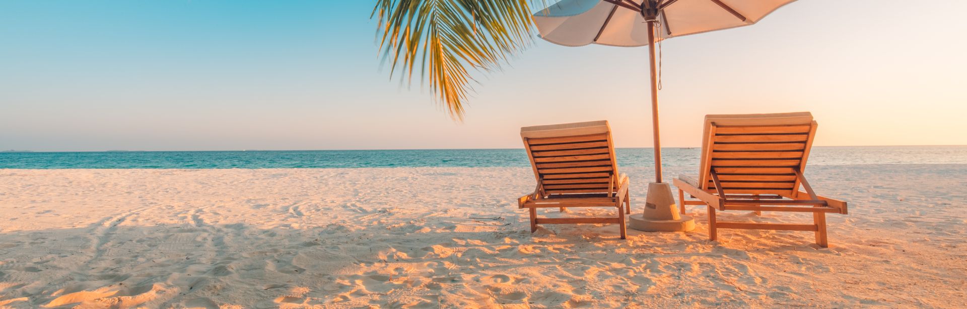 Zwei Liegen mit einem Sonnenschirm stehen unter Palmen am Strand