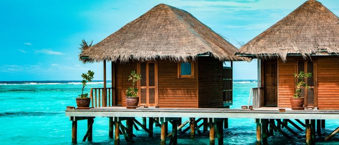 Zwei strohgedeckte Holzhütten stehen auf Stelzen über dem Meer.