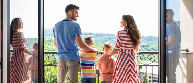 Eine Familie mit zwei Kindern steht Arm in Arm auf einem Balkon 