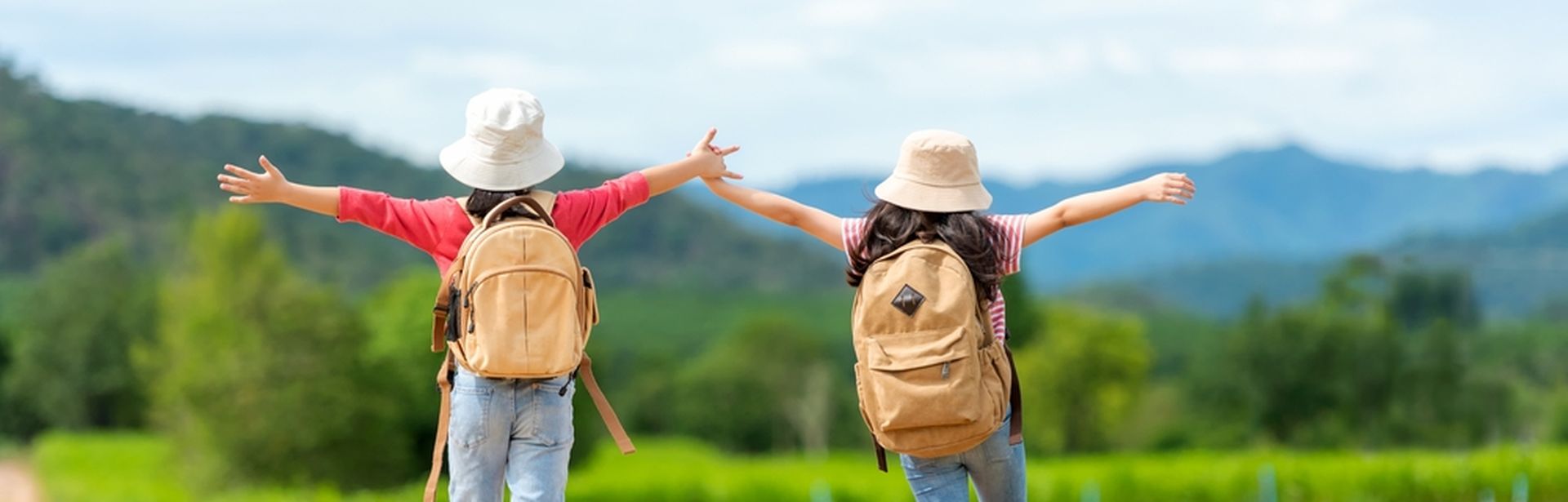Zwei Mädchen mit Rucksäcken laufen fröhlich einen Weg entlang und heben die Arme in die Luft