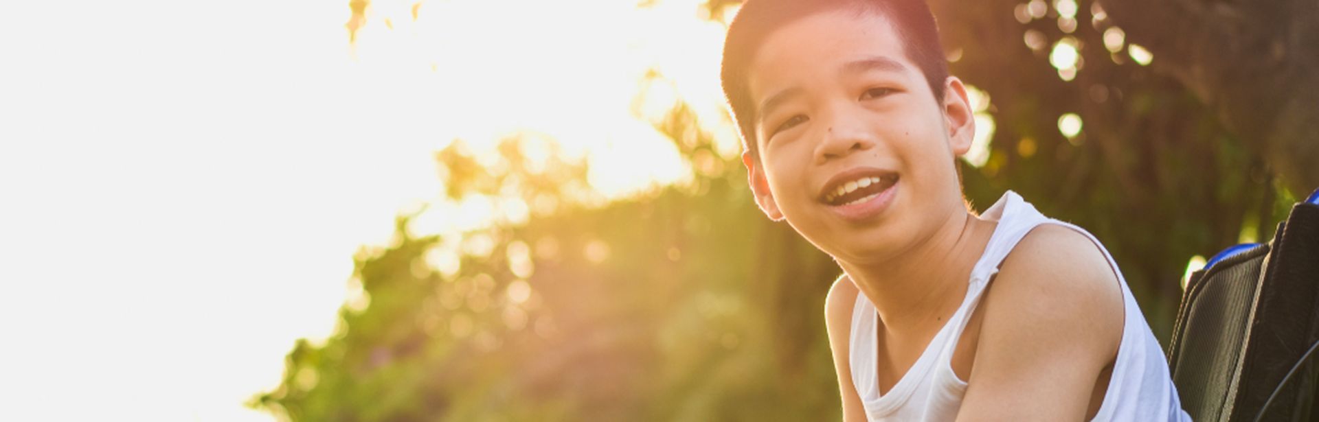 Junge im Rollstuhl in der Natur lächelt in die Kamera