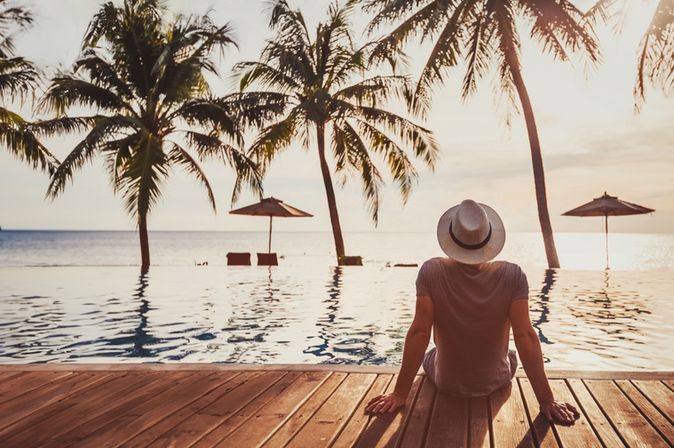 Mann sitzt auf einem Steg am Wasser und schaut in die Sonne