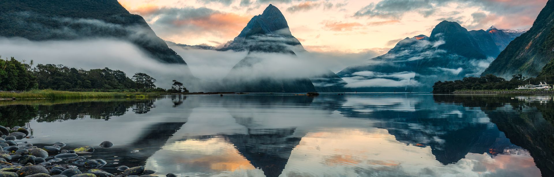 Runde Steine, die in einen See führen im Hintergrund sind von Nebel umzogene Berge zu sehen, die sich im Wasser spiegeln