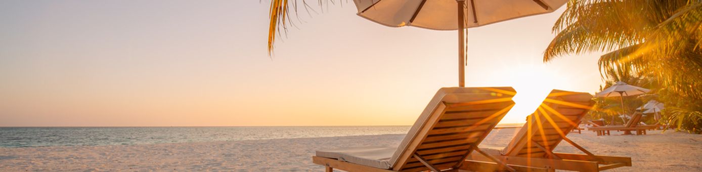 Zwei Liegen unter einem Schirm am Strand