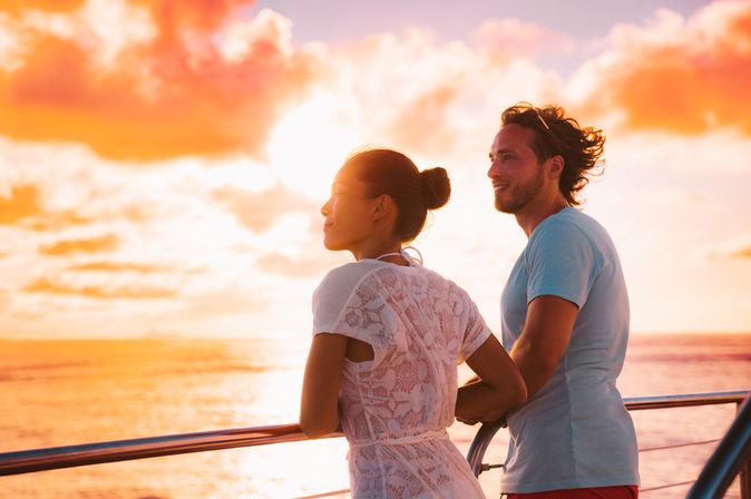 Eine Frau und ein Mann stehen bei Sonnenuntergang an der Reling eines Kreuzfahrtschiffes