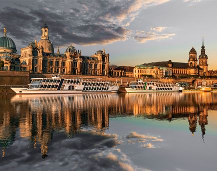 Flusskreuzfahrschiffe fahren an alten Bauwerken vorbei, die sich im stillen Wasser des Flusses spiegeln