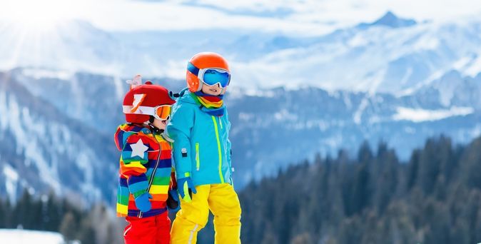 Zwei Kinder stehen auf Skiern vor einer verschneiten Berglandschaft