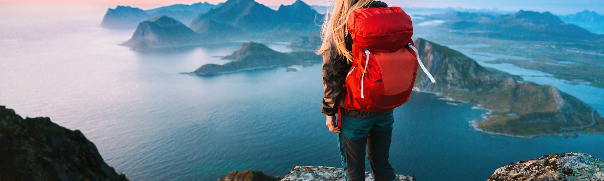 Alleinreisende Frau mit Rucksack schaut von einem Berg auf Wasser 
