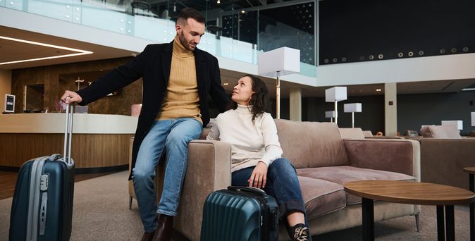 Eine Frau und ein Mann sitzen mit Koffern in einer Lobby und schauen sich an