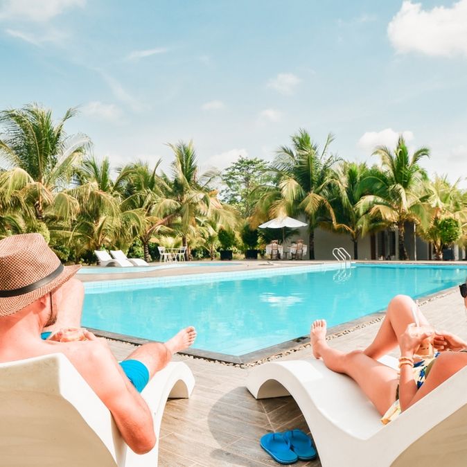 Eine Frau und ein Mann liegen auf weißen Liegen am Pool und trinken jeweils ein Getränk