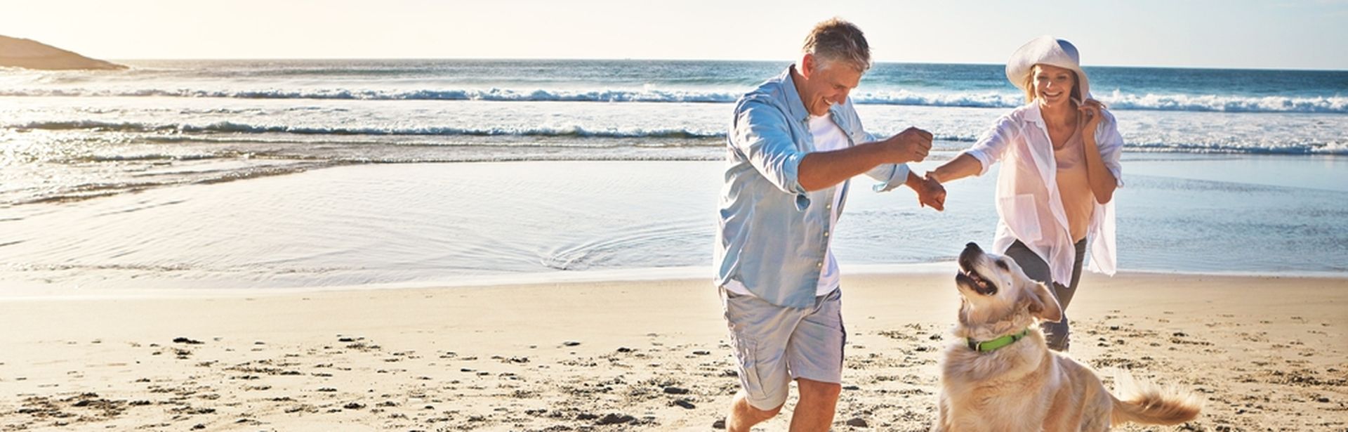 Eine Frau und ein Mann spielen am Strand mit einem Hund 