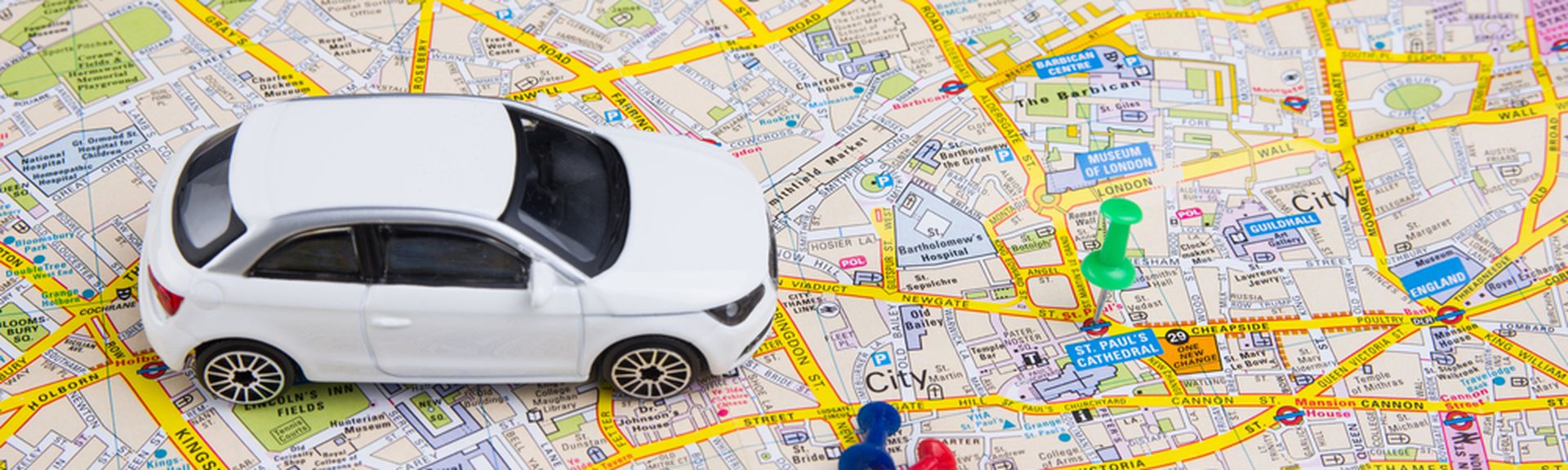 Ein Miniaturauto steht auf einer Stadtkarte von London. Daneben zwei Reißzwecken