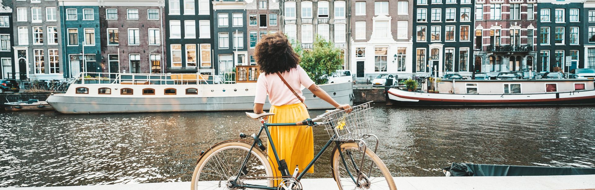 Frau mit Fahrrad schaut auf Häuser in Amsterdam