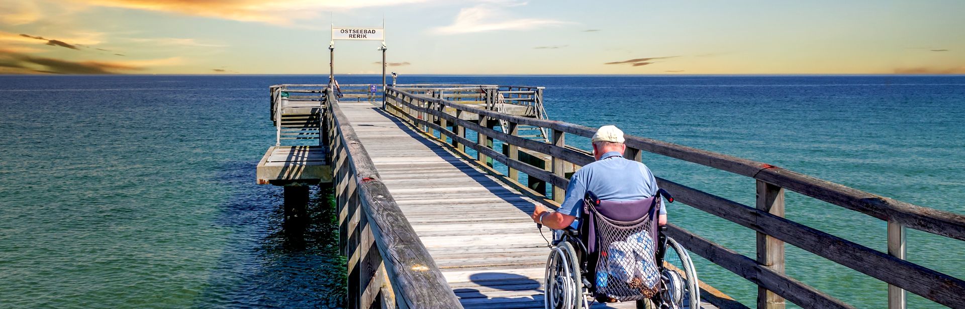Mann im Rollstuhl auf einer Seebrücke am Meer