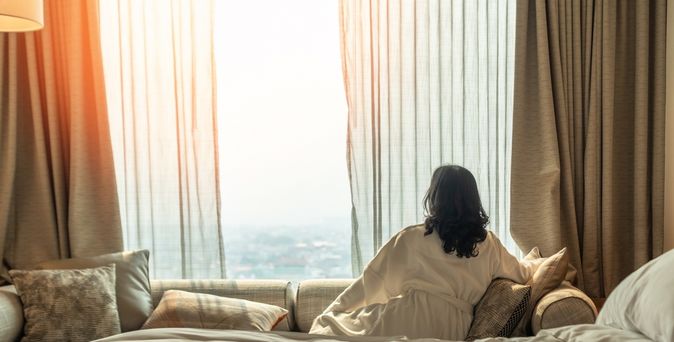 Frau im Bademantel sitzt im einem Hotelzimmer auf dem Sofa und schaut aus dem Fenster