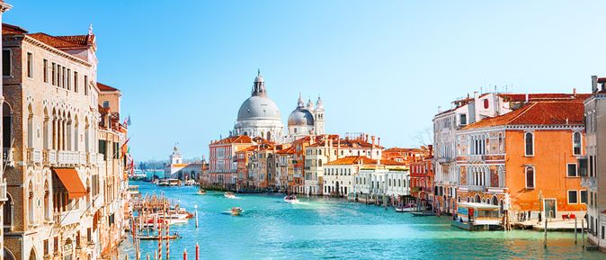 Blick auf den Canal Grande in Venedig, Italien. Links und rechts stehen historische Gebäude. Auf dem türkisblauen Wasser fahren kleine Boote.
