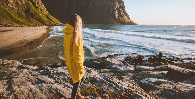 Eine Frau in einer gelben Regenjacke schaut auf das Meer