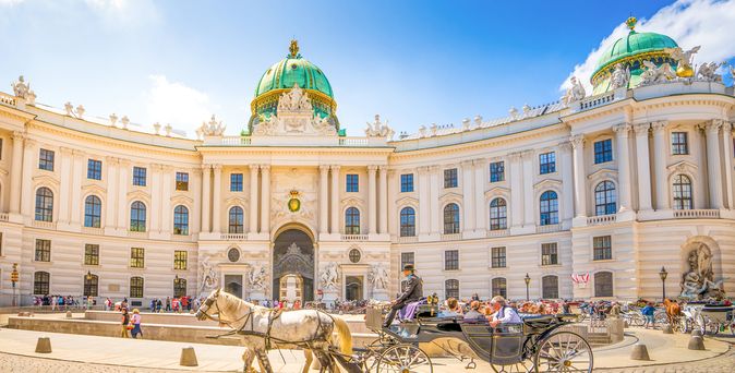 Pferdekutsche vor der Hofburg in Wien, Österreich, an einem sonnigen Tag. Im Hintergrund laufen viele Touristen über den Platz.