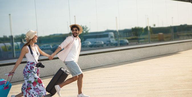 Ein Paar läuft mit Koffern aufgeregt einen Weg entlang