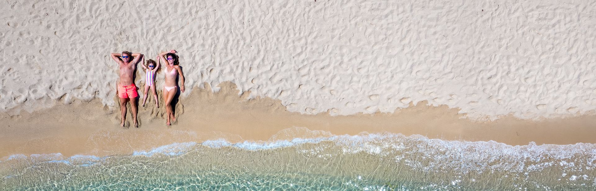 Bild vom Strand aus der Vogelperspektive. Auf dem Strand liegt eine Familie mit einem Kind