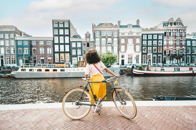 Frau mit Fahrrad schaut auf Häuser in Amsterdam