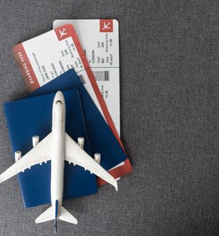 Ein Miniaturflugzeug liegt auf einem Reisepass in dem sich zwei Flugtickets befinden