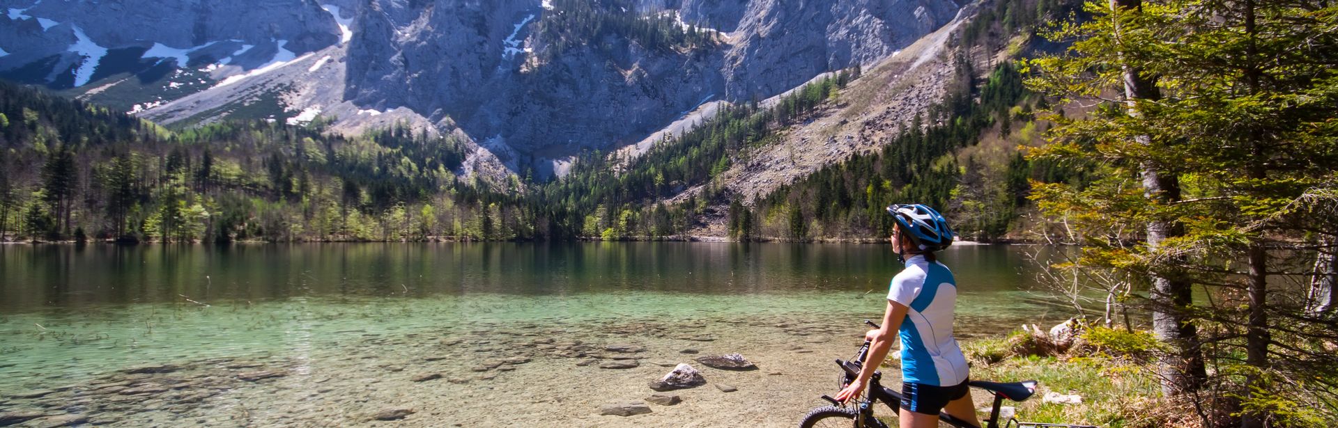 Eine Frau bestaunt auf dem Fahrrad Berge und einen See