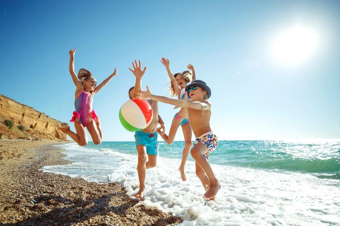 Eine Gruppe von Kindern spielt mit einem Ball am Strand und springen alle in die Luft