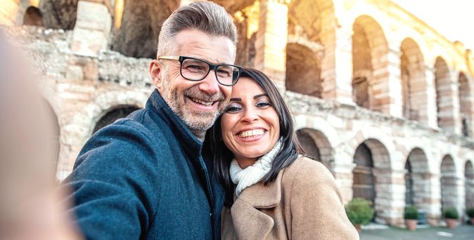 Ein Paar macht vor einem Bauwerk ein Selfie und lächelt in die Kamera