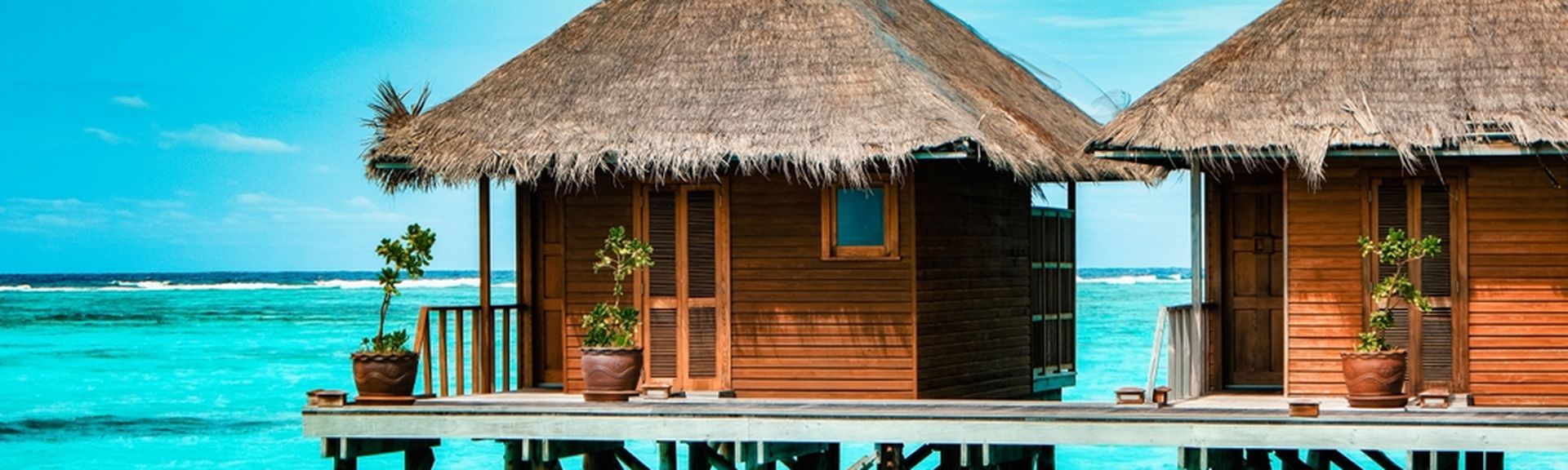 Zwei strohgedeckte Holzhütten stehen auf Stelzen über dem Meer.