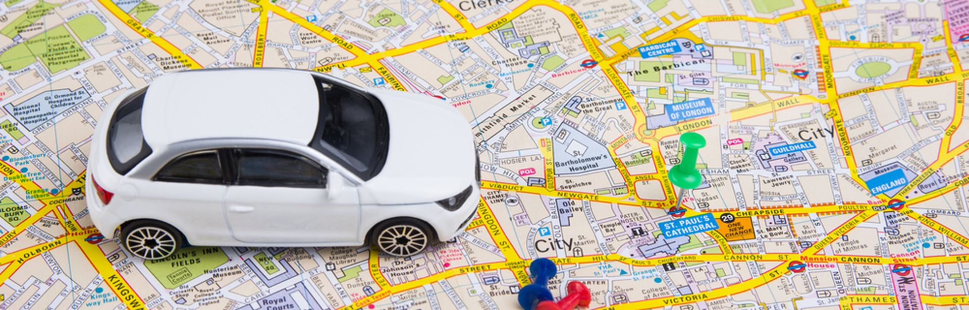 Ein Miniaturauto steht auf einer Stadtkarte von London. Daneben zwei Reißzwecken