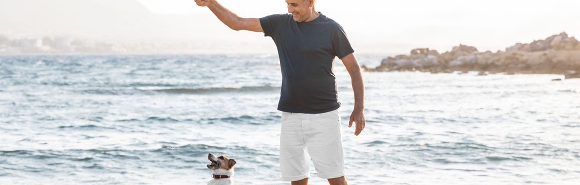 Ein Mann und ein Hund spielen Stöckchen holen am Strand