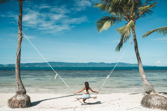 Frau auf einer Schaukel zwischen zwei Palmen am Meer