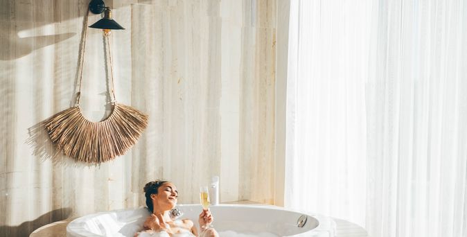 Eine Frau sitzt in einem Whirlpool in einem modernen Hotelzimmer und trinkt ein Glas Sekt