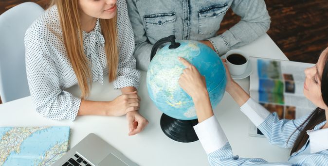 Ein Paar sitzt mit einer Reiseberaterin am Tisch, während die Reiseberaterin dem Paar etwas auf einem Globus zeigt