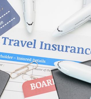 In der Mitte des Bildes steht "Travel Insurance" darum liegen mehrere Büroklammern, Reisepässe und mehrere kleine Flugzeuge