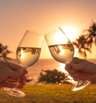 Zwei Gläser stoßen vor einem Sonnenuntergang am Strand an