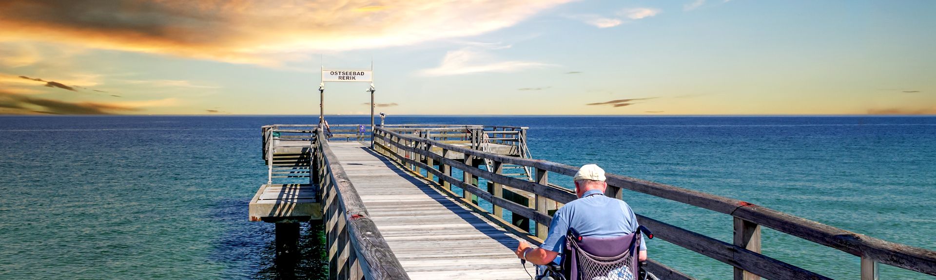 Mann im Rollstuhl auf einer Seebrücke am Meer