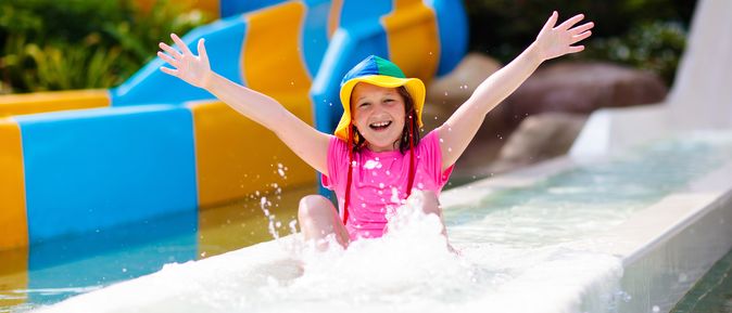 Ein glücklich aussehendes Kind rutscht durch eine Wasserrutsche und hebt die Arme