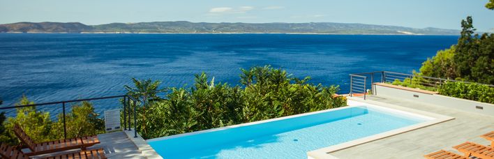 Ein Privatpool über dem Meer, um ihn herum einige Holzliegen und Bäume