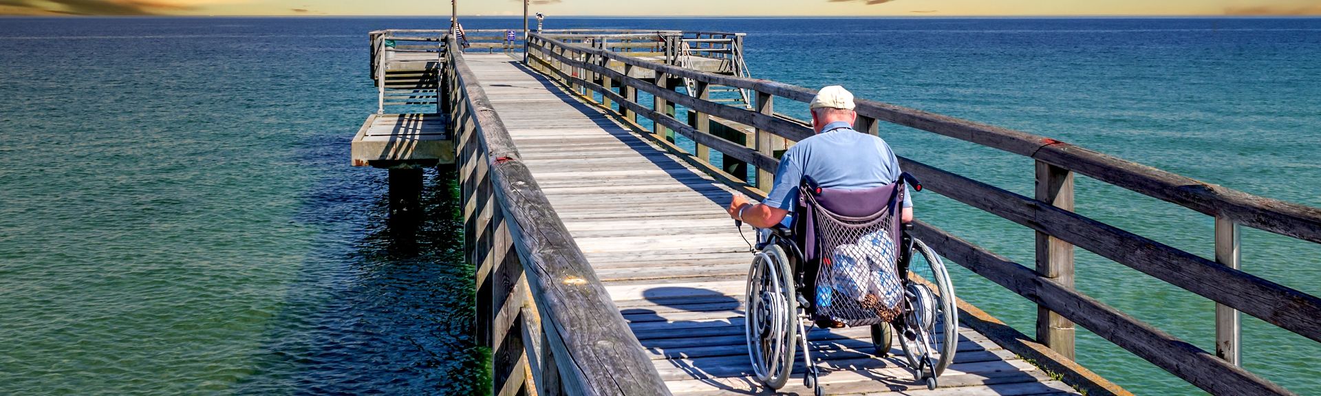 Mann im Rollstuhl auf einer Seebrücke am Meer
